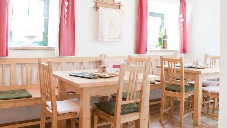 Gem&uuml;tlicher Gastraum mit Holzm&ouml;beln, roten Vorh&auml;ngen und Dekoration.