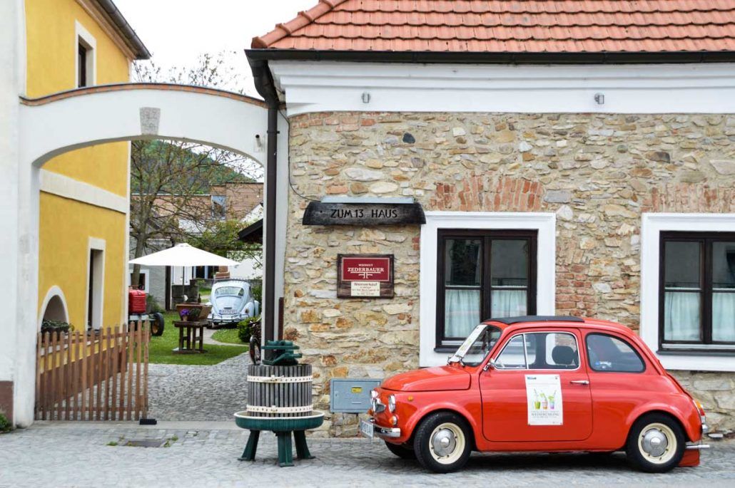 Eingang zu einem Heurigen mit einem roten Oldtimer und einem gelben Gebäude.