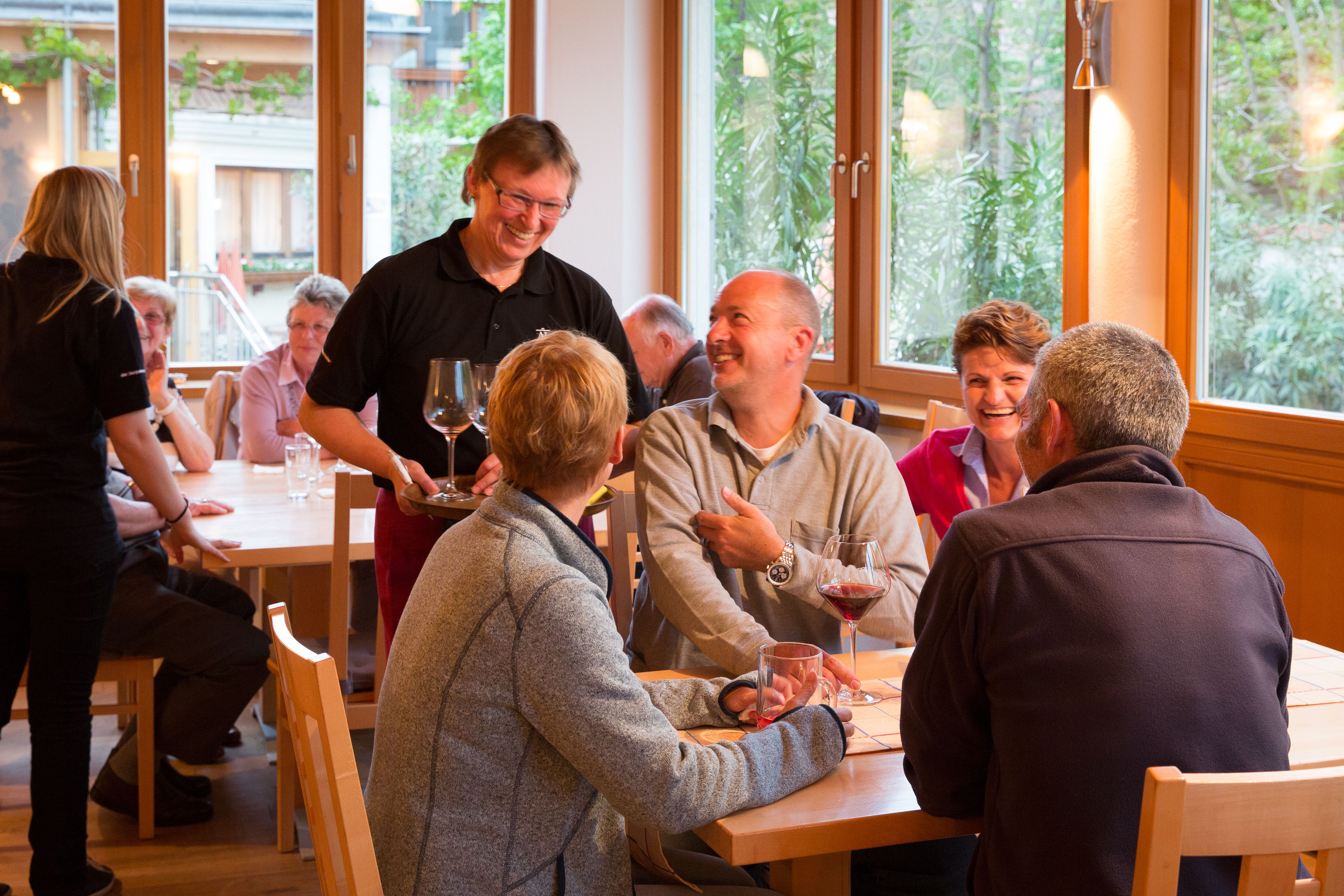 Menschen in einem gemütlichen Restaurant, die Wein trinken und lachen.