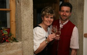 Zwei Personen in traditioneller Kleidung sto&szlig;en mit Weingl&auml;sern an.