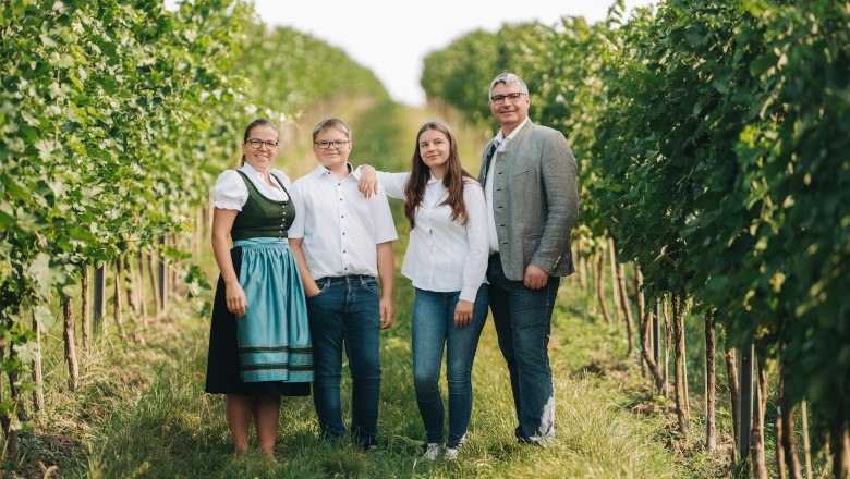 Eine Familie steht l&auml;chelnd in einem Weinberg.